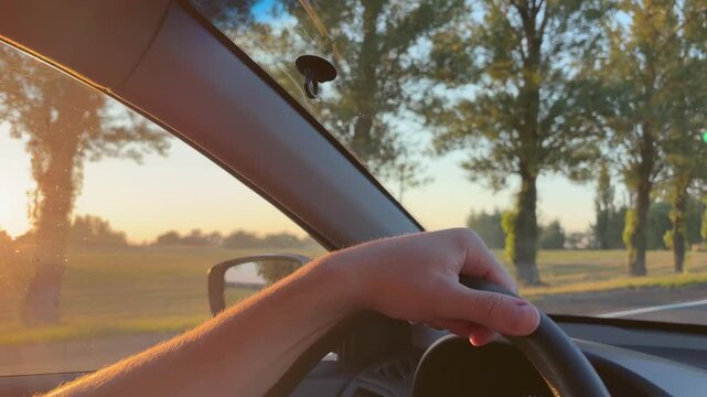 Countryside trip. A driver's hand on the steering wheel driving through the countryside at sunset