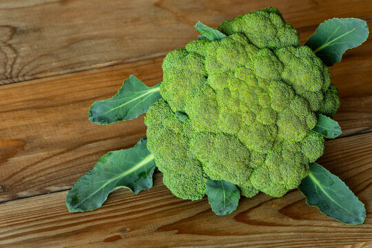 Garden-fresh broccoli head with leaves against wooden boards in studio: raw broccoli, rustic wood, and natural light.
