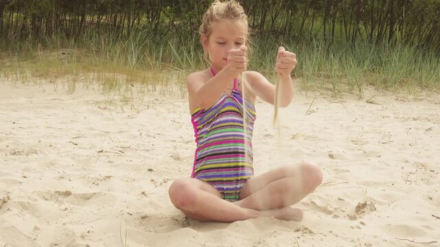Little beautiful girl pours sand on shore of sea
