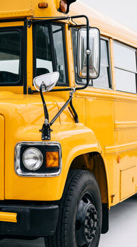 Close-up of a bright yellow school bus front, showcasing its headlight, mirror, and tire, symbolizing education, travel, and community transport.
