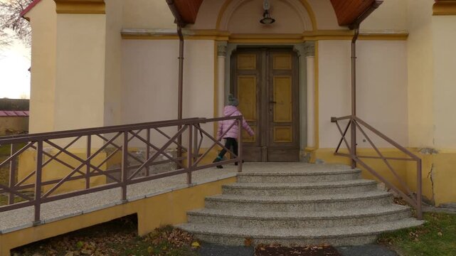 Little beautiful girl in pink jacket walks near Church St. Stefan Uhorskeho, Janovce-Cencice, Slovakia.