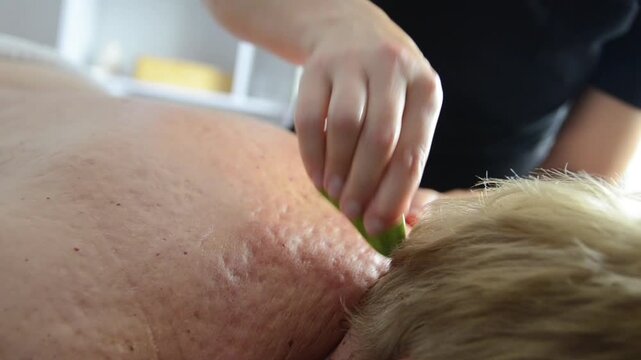 Massage therapist performs gua sha massage on a woman&rsquo;s back using a stone tool. Close-up body treatment focused on relaxation and muscle care.
