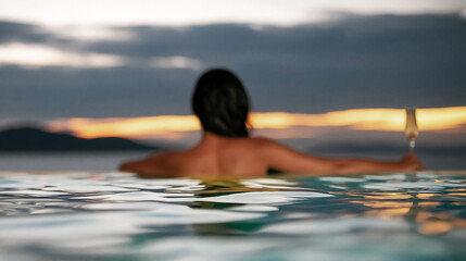 Fototapeta premium Woman relaxing alone in an infinity pool overlooking the ocean at sunset, enjoying a luxury travel experience with a drink