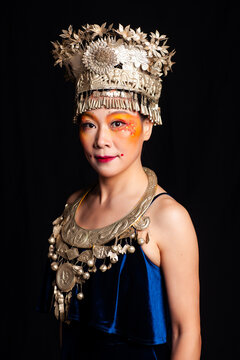 A portrait of an oriental woman wearing ornate Miao silver jewelry against a black background.