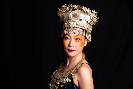 A portrait of an oriental woman wearing ornate Miao silver jewelry against a black background.