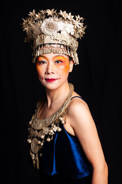 A portrait of an oriental woman wearing ornate Miao silver jewelry against a black background.