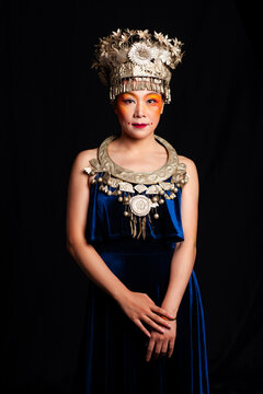 A portrait of an oriental woman wearing ornate Miao silver jewelry against a black background.