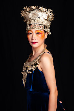 A portrait of an oriental woman wearing ornate Miao silver jewelry against a black background.