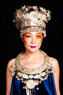 A portrait of an oriental woman wearing ornate Miao silver jewelry against a black background.