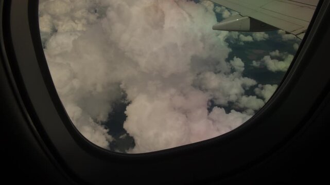 Passenger view through airplane window of aircraft wing flying beside large cumulus clouds above countryside