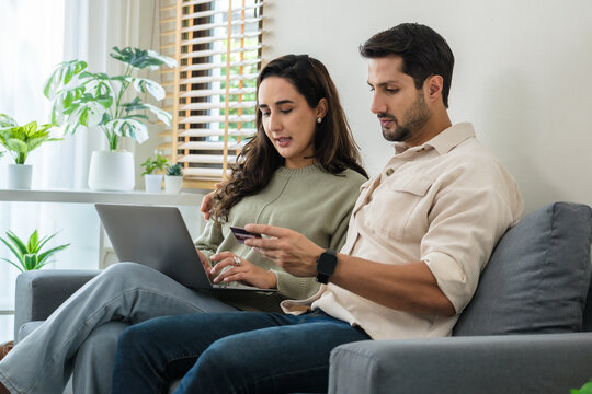 Happy couple using credit card and laptop at home for seamless online shopping experience with smartphone