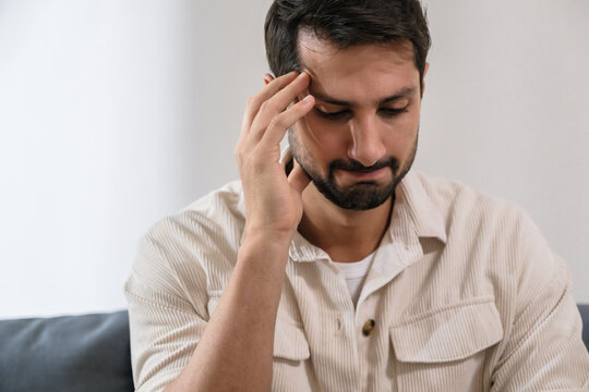 Sad anxious man feeling stress and depression while sitting alone on sofa, suffering emotional problem and mental frustration at home