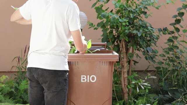 Man disposing of organic garden waste and trimmed branches into a brown bio compost bin