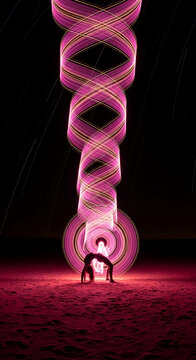 Light painting of a person in a bridge pose creating pink and gold swirling vortexes, symbolizing creativity, motion, and ephemeral art on a sandy surface.