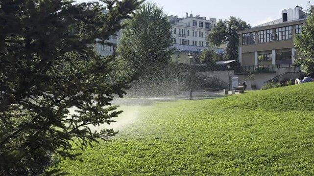 Moscow, Russia, August 3, 2026: Water fountain sprinkling a green lawn in Ivanovskaya Gorka Park on a sunny summer day. Bright sunlight and fresh water spray create a peaceful urban park atmosphere.

