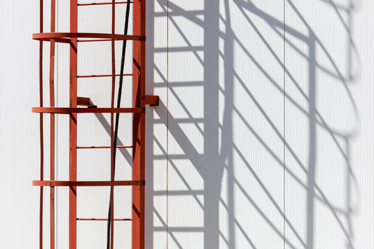 Red ladder casts sharp shadow on white wall