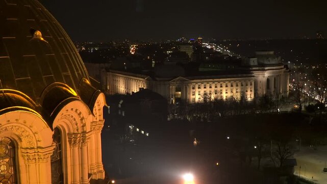Static elevated night view of Sofia University in central Sofia, with its illuminated Rectorate facade, city lights and the Alexander Nevsky Cathedral dome in the foreground.