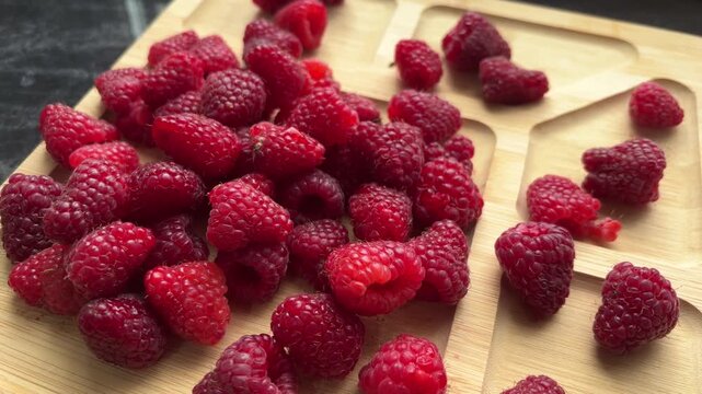 Close view of ripe raspberries on a wooden serving tray, fresh berry texture, healthy summer food, seasonal harvest, natural fruit background.