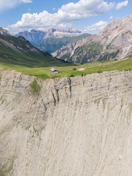 Pozza di Fassa, Italy - 11 July 2026: Aerial view of a mountain refuge perched on a dramatic cliff edge overlooking a lush alpine valley with rugged mountain peaks in the background.