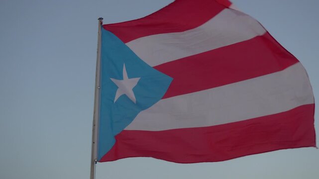 Cinematic stock footage of the Puerto Rican flag waving dynamically in the wind against a clear sky. Perfect for patriotic, cultural, and political video projects.
