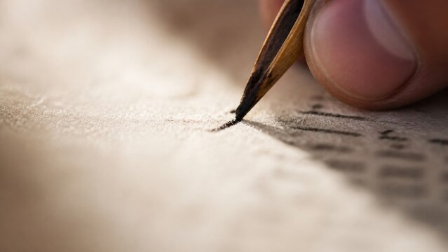 Close-up of a hand writing a small mark on an ancient scroll. Biblical law, scripture, enduring faith, and the unchanging word of God.