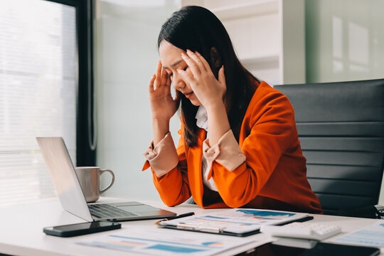 Office Discomfort: A female office worker in a red shirt experiences neck pain while working on her laptop, surrounded by office supplies and a calculator, indicating a stressful work environment.
