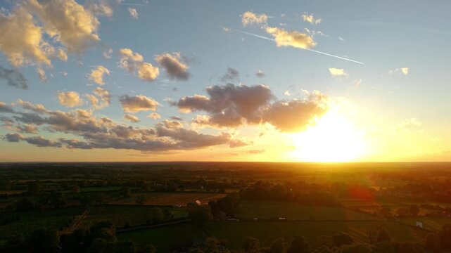 Evening sunlight over countryside fields and rural villages. Golden hour sky filled with dramatic clouds above farmland horizon. Warm sunset glow illuminating agricultural landscape across open