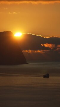 Sunset boat ocean silhouette against a dramatic golden sky with sun peeking over a high cliff at dawn or dusk