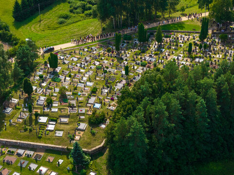 Juzintai, Lithuania - 26 July 2026: Aerial view of the cemetery in Juzintai, with numerous gravestones set in green lawns near a forest and people walking on a path.