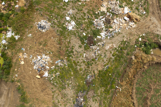Top down aerial view of illegal trash and plastic waste dumped on open green fields and soil under bright daylight, highlighting environmental pollution and ecological damage issues.