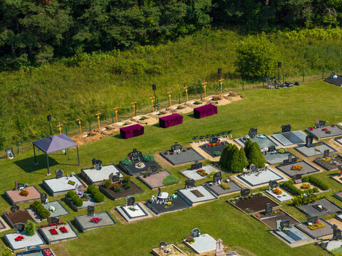 Juzintai, Lithuania - 26 July 2026: Aerial view of a cemetery with numerous gravestones, manicured green lawns, and a row of wooden crosses in a rural setting.