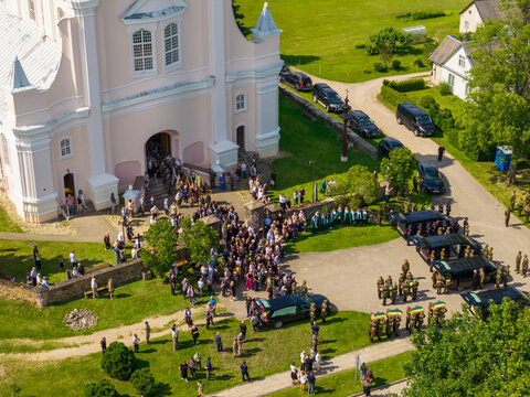 Juzintai, Lithuania - 26 July 2026: Aerial view of a funeral procession at the Church of St. Michael the Archangel with military personnel and mourners gathered on the grounds.