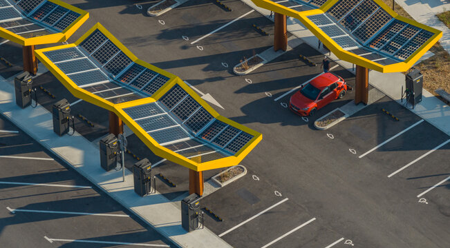 Saulce-sur-Rhone, France - 28 July 2026: Aerial view of the Fastned electric vehicle charging station with yellow solar canopies, charging infrastructure, and an electric car.