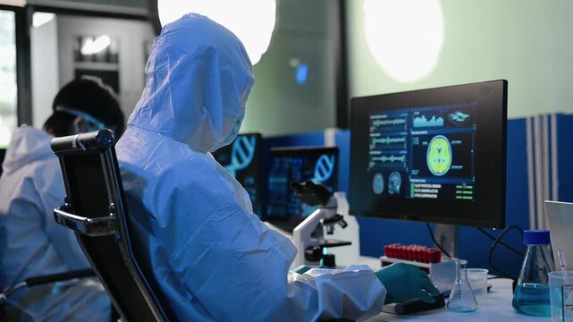 Scientists in protective hazmat suits analyze brain scan data, MRI diagnostics, and neural analytics on dual monitors in a high tech modern medical laboratory