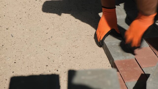 Municipal construction worker quickly lays paving tiles on a sidewalk base. Municipal improvement, public works, urban infrastructure, sidewalk construction and migrants in the workforce