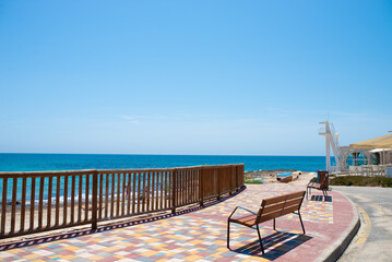 Colorful seaside promenade with wooden railing and benches overlooking a sandy beach and blue Mediterranean Sea under a clear summer sky. © ольга дубровная