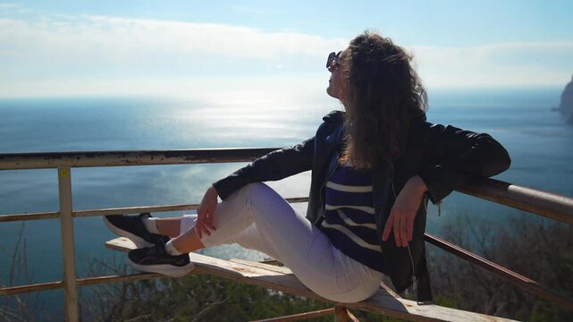 Woman ocean relaxing sitting on a scenic overlook bench with views of the vast blue sea on a sunny spring day