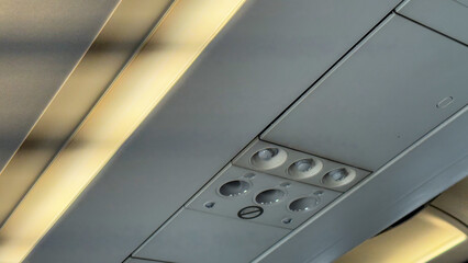 Overhead airplane cabin interior showing ventilation vents, reading lights, and luggage compartments during a flight © svetograph