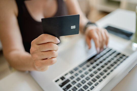 Person enters bank card details into laptop to complete online purchase from home during daytime