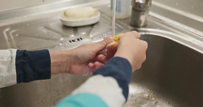 Kid hands wash peach under tap water in sink. Boy help in kitchen. 4K 10-bit