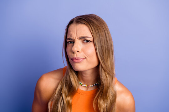 Young chic woman with orange singlet puzzled look against blue background