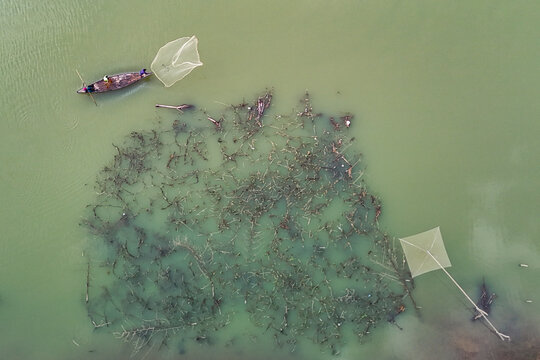 Sherpur District, Mymensingh Division, Bangladesh - 21 November 2024: Aerial view of Bhugai River with fishermen in a boat casting nets over submerged branches.