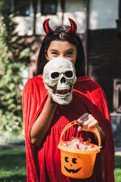 Cute kid dressed as devil for Halloween near spooky decorated house
