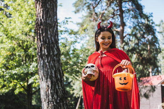 Charming child in devil costume enjoys Halloween near a festively decorated home