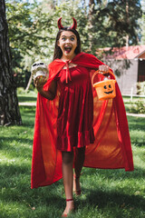 Fototapeta premium Cute kid excited for Halloween in a devil costume near spooky decorated house