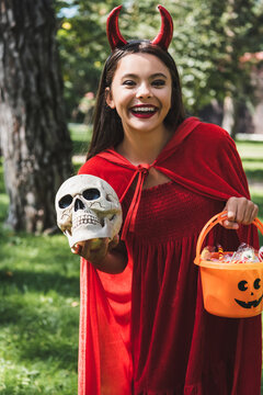 Joyful child in a devil costume enjoying Halloween near a spooky decorated house