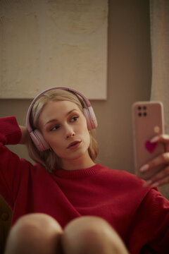 Young Caucasian woman wearing headphones and holding smartphone, taking selfie or streaming content. Image represents digital lifestyle, perfect for social media marketing, vertical