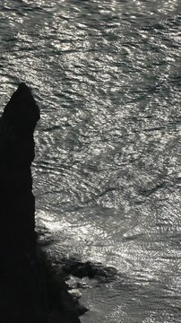 Ocean cliff shimmer silhouette of a rugged rock against sparkling water waves creating a moody and atmospheric coastal landscape