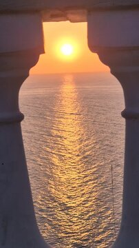 Golden sunset ocean views frame through stone architectural columns at dusk near the sea coast. Vertical static shot.