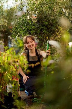 Smiling Gardener Watering Plants in Greenhouse Nursery Wearing Apron, Plant Care and Small Business